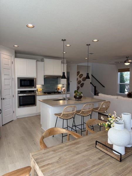 A modern kitchen with sleek white cabinets, an island, and pendant lighting, flowing into an open dining area with natural wood accents. 