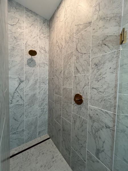 A sleek shower featuring luxurious marble tiles and elegant gold fixtures for a touch of modern sophistication.