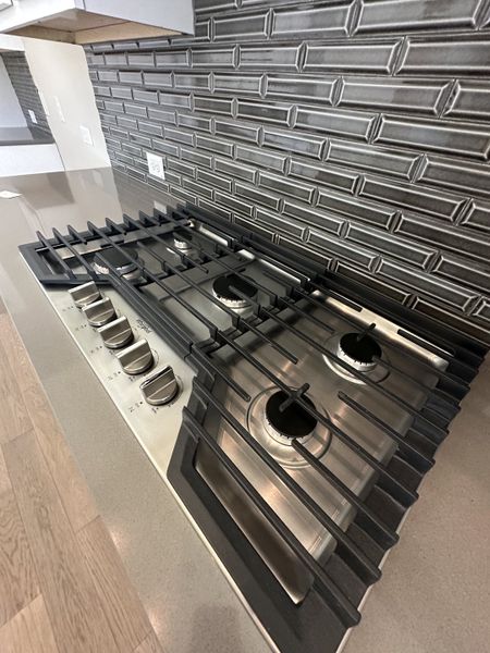A sleek kitchen with a modern gas cooktop, elegant gray backsplash, and wooden flooring. A sleek kitchen with a modern gas cooktop, elegant gray backsplash, and wooden flooring.