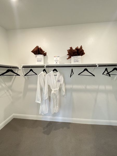 A spacious walk-in closet with dual hanging rods and cozy white robes, featuring elegant carpeting.