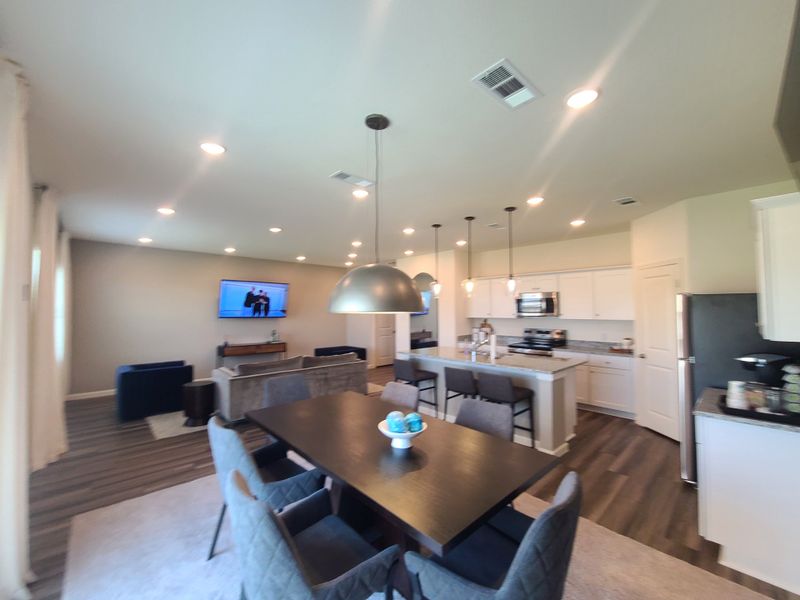 An open-concept kitchen and living area with modern lighting, dark wood floors, and sleek white cabinetry. An open-concept kitchen and living area with modern lighting, dark wood floors, and sleek white cabinetry.