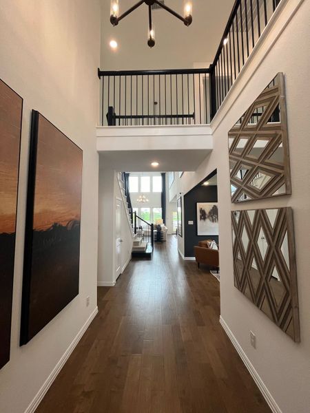 An elegant foyer with wooden floors, high ceilings, modern chandelier, and artistic wall decor, leading to a bright living area.