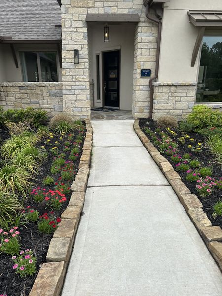A charming stone exterior with lush landscaping in Stewart’s Forest by Sitterle Homes (Conroe, TX).