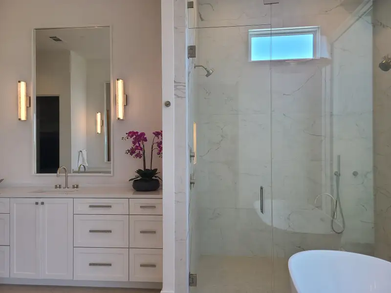 A modern bathroom featuring a sleek glass shower, white cabinetry, and elegant lighting fixtures.