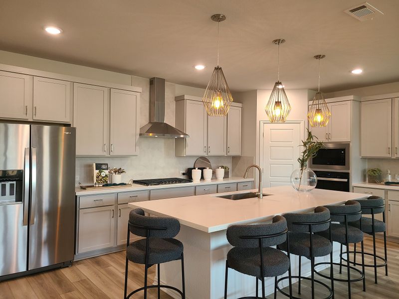 A modern kitchen featuring white cabinets, a central island with sleek seating, stainless steel appliances, and stylish lighting.