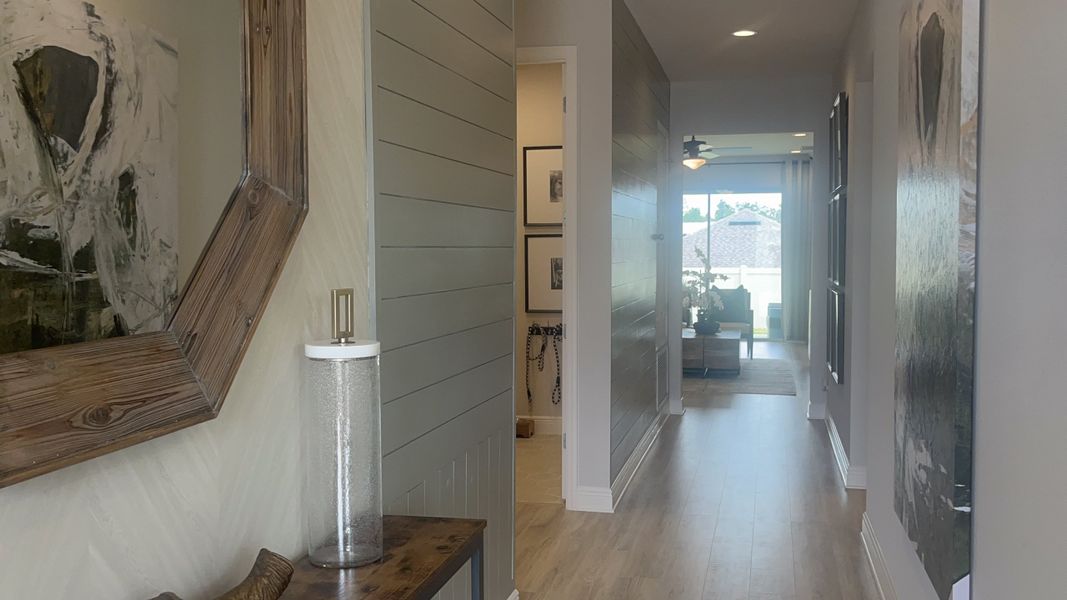 A modern hallway with wood accents, large mirror, stylish decor, and natural light guiding towards the living area.