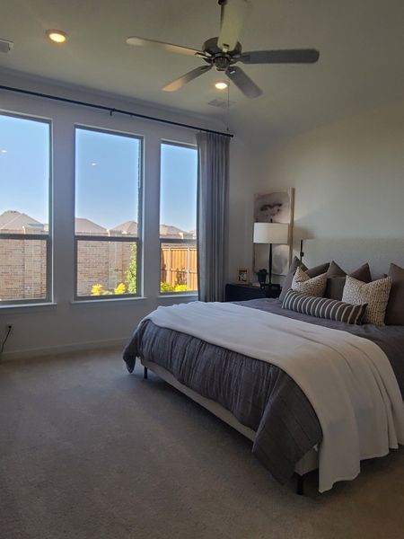 A cozy bedroom with a large window, neutral bedding, soft carpeting, and a ceiling fan for a relaxing ambiance. A cozy bedroom with a large window, neutral bedding, soft carpeting, and a ceiling fan for a relaxing ambiance.