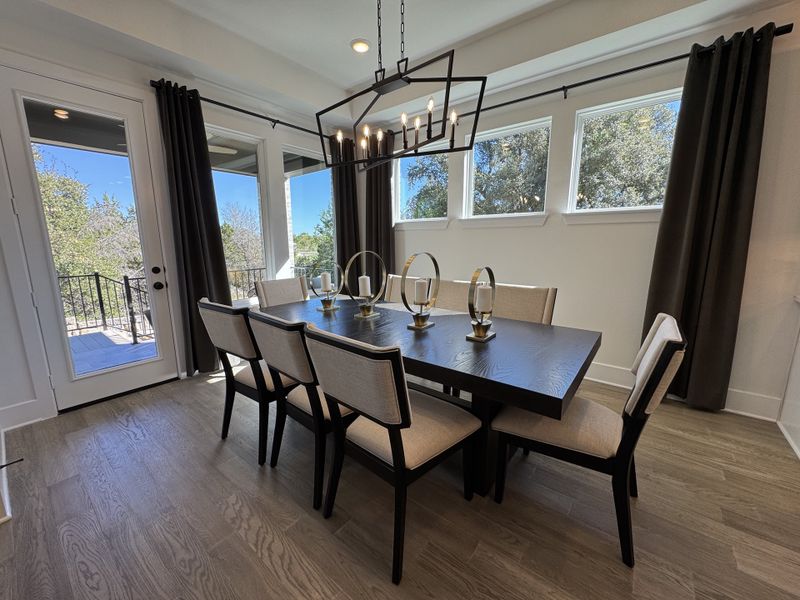 A chic dining area featuring a sleek dark wood table, elegant chairs, and large windows offering scenic views.