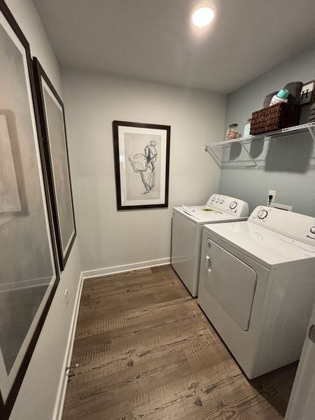 A cozy laundry room with framed artwork, wood flooring, and a washer-dryer set.