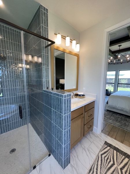 A modern bathroom with blue-tiled rain shower, wood vanity, elegant lighting, and marble-look flooring. A modern bathroom with blue-tiled rain shower, wood vanity, elegant lighting, and marble-look flooring.