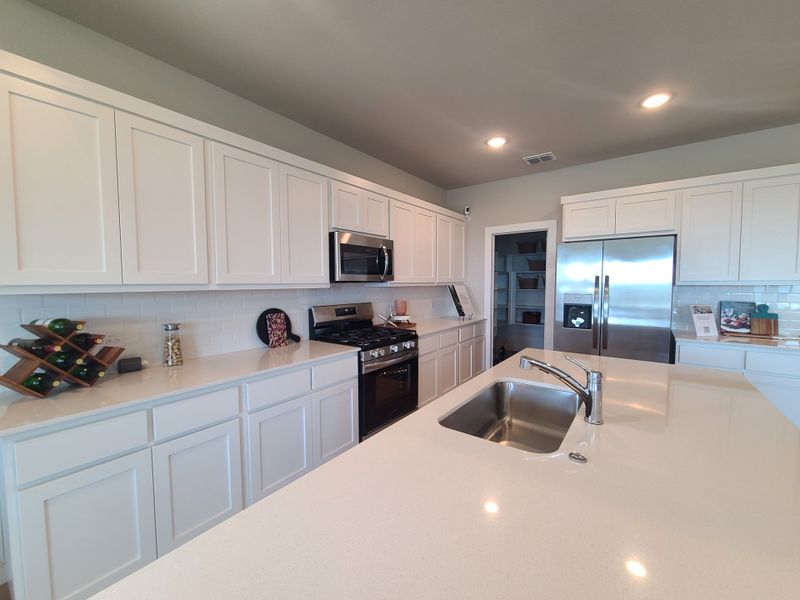 A modern kitchen with sleek white cabinetry, stainless steel appliances, and a spacious island with a sink. A modern kitchen with sleek white cabinetry, stainless steel appliances, and a spacious island with a sink.