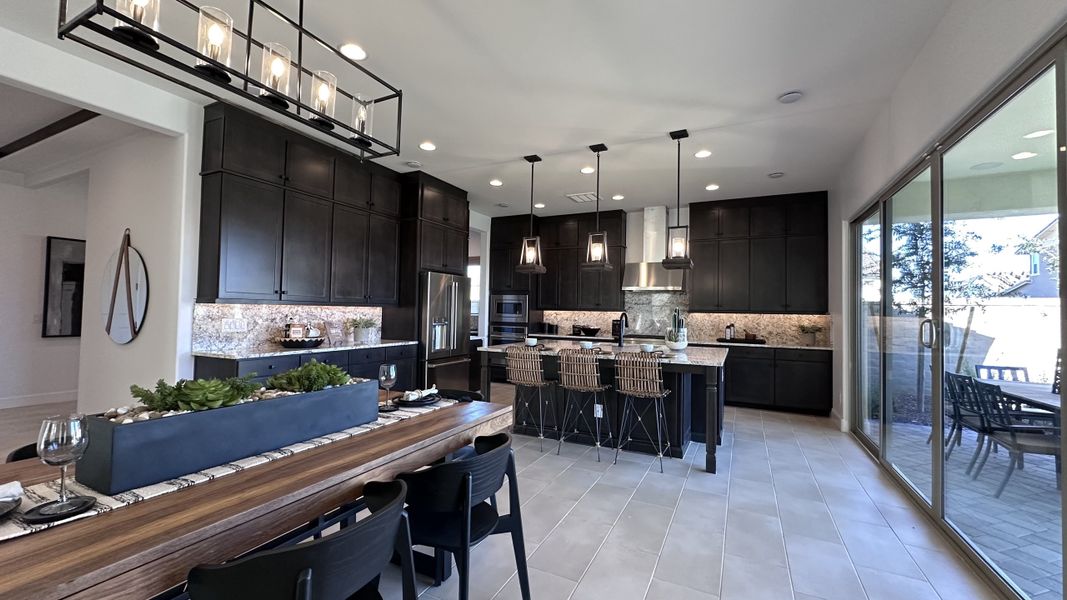 A modern kitchen with dark cabinets, granite countertops, an island, and pendant lighting. Large sliding doors offer ample light.