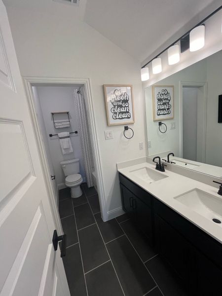 A sleek bathroom with dark floor tiles, dual sinks, a modern mirror, and stylish decor. A sleek bathroom with dark floor tiles, dual sinks, a modern mirror, and stylish decor.