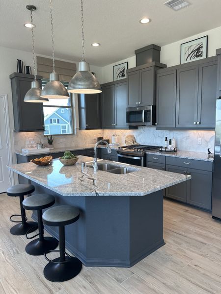 A modern kitchen with sleek gray cabinets, a granite island, and stylish pendant lighting. A modern kitchen with sleek gray cabinets, a granite island, and stylish pendant lighting.