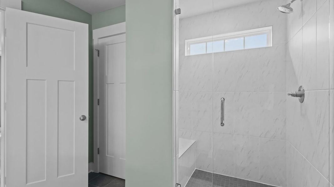 DRB Homes' Woodglen offering a luxe primary bathroom with a stunning marble tiled, frameless walk-in shower with bench seat