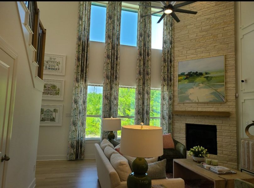 A spacious living room with high ceilings, tall windows, a brick fireplace, and elegant decor.