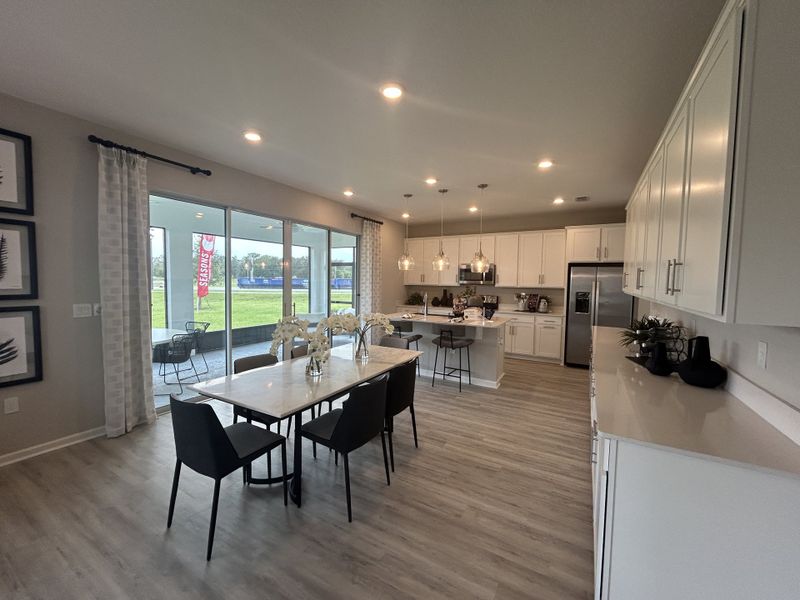 A spacious kitchen and dining area with sleek white cabinets, modern lighting, and large windows to a patio view. A spacious kitchen and dining area with sleek white cabinets, modern lighting, and large windows to a patio view.