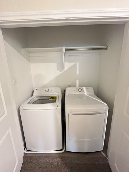 A convenient laundry nook featuring a modern washer and dryer set, with shelving and hanging space.