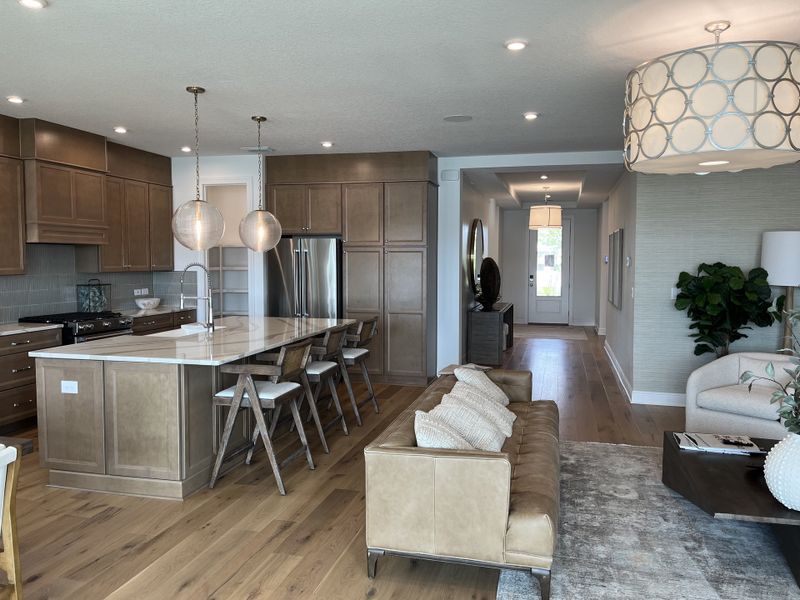 A contemporary kitchen with wood cabinetry, sleek island seating, and stylish pendant lights. Comfortable seating area nearby.