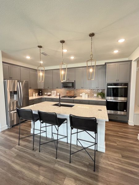 A modern kitchen featuring gray cabinets, a large island with marble countertops, pendant lighting, and stainless steel appliances. A modern kitchen featuring gray cabinets, a large island with marble countertops, pendant lighting, and stainless steel appliances.