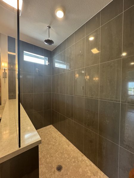 A spacious walk-in shower with sleek gray tiles, pebble mosaic floor, and a modern rain showerhead.