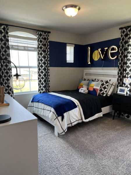 A cozy bedroom with vibrant decor, featuring a stylish bed, patterned curtains, and playful wall art.