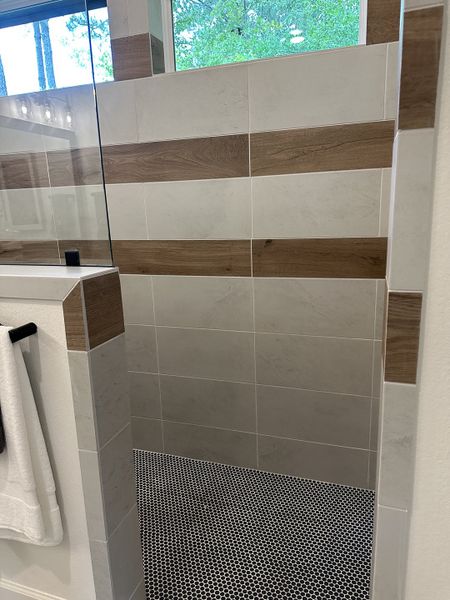 A modern shower with wood-accented tiles and a pebble mosaic floor, offering a serene and stylish bathing experience.