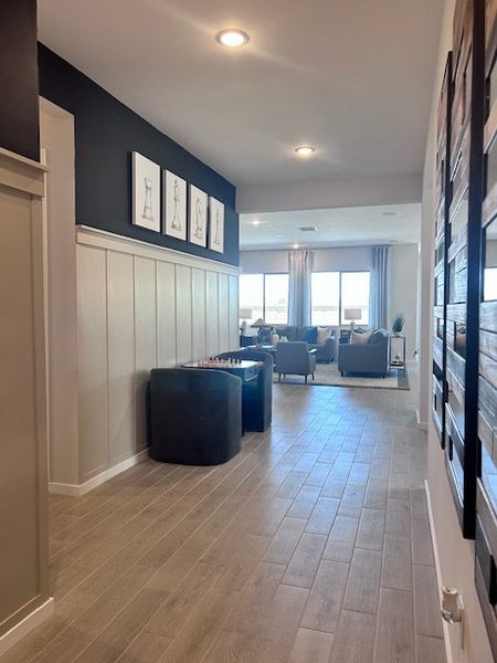 A welcoming hallway with wood flooring, modern art, and a cozy living area featuring large windows and comfortable seating. A welcoming hallway with wood flooring, modern art, and a cozy living area featuring large windows and comfortable seating.