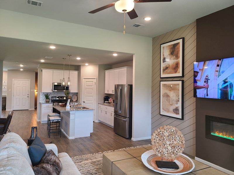 An open-concept living space with a modern kitchen, artwork, and cozy fireplace alcove, featuring contemporary decor and lighting.