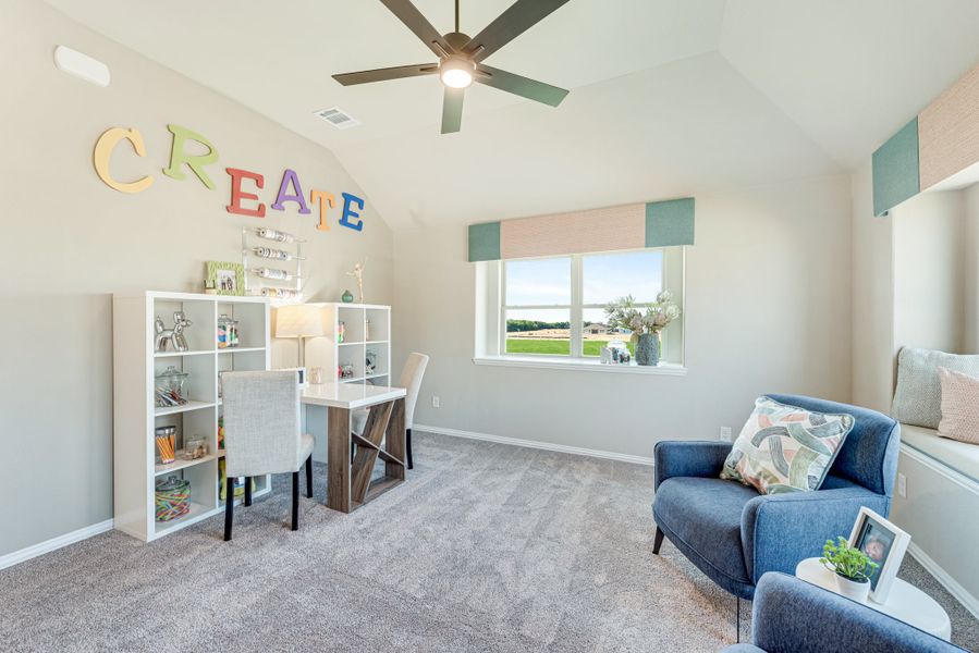 Kids' craft room with vaulted ceiling, white shelving unit, desk, and blue seating area on gray carpet