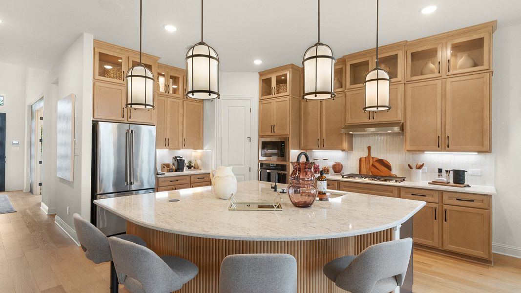 Modern kitchen with ceiling-height cabinets, built-in appliances, statement lighting, and a large center island.