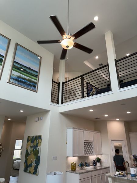 A modern living space with high ceilings, a sleek ceiling fan, and an elegant open loft above a bright kitchen.
