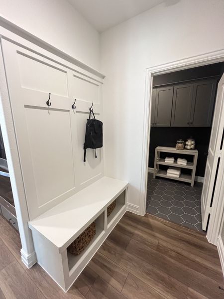 A contemporary mudroom with a bench, hooks, and storage, leading into a hexagon-tiled laundry room. A contemporary mudroom with a bench, hooks, and storage, leading into a hexagon-tiled laundry room.