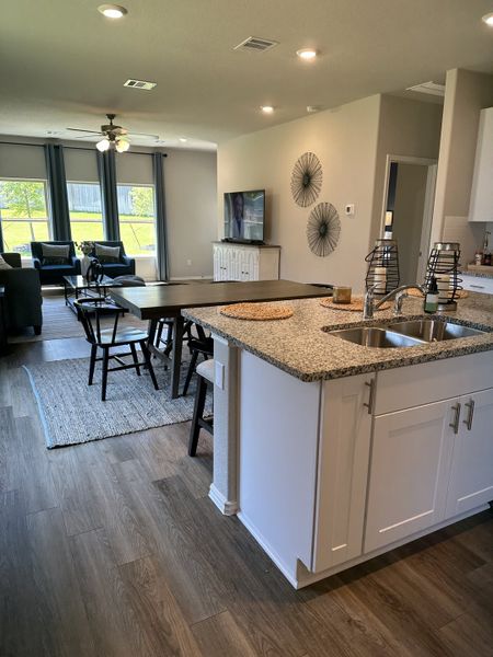 An open-concept living area featuring wood floors, a granite kitchen island, and a cozy seating area with large windows.