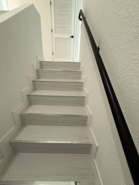 A modern staircase with sleek white steps and a black handrail leading to a louvered door.