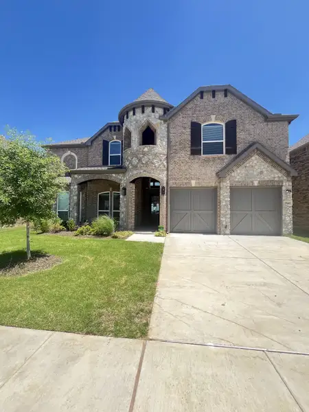 A stunning brick and stone home with elegant details and a manicured lawn in Polo Ridge by First Texas Homes (Forney, TX).