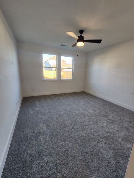 A spacious bedroom with soft gray carpeting, white walls, and a ceiling fan, perfect for comfort and relaxation.