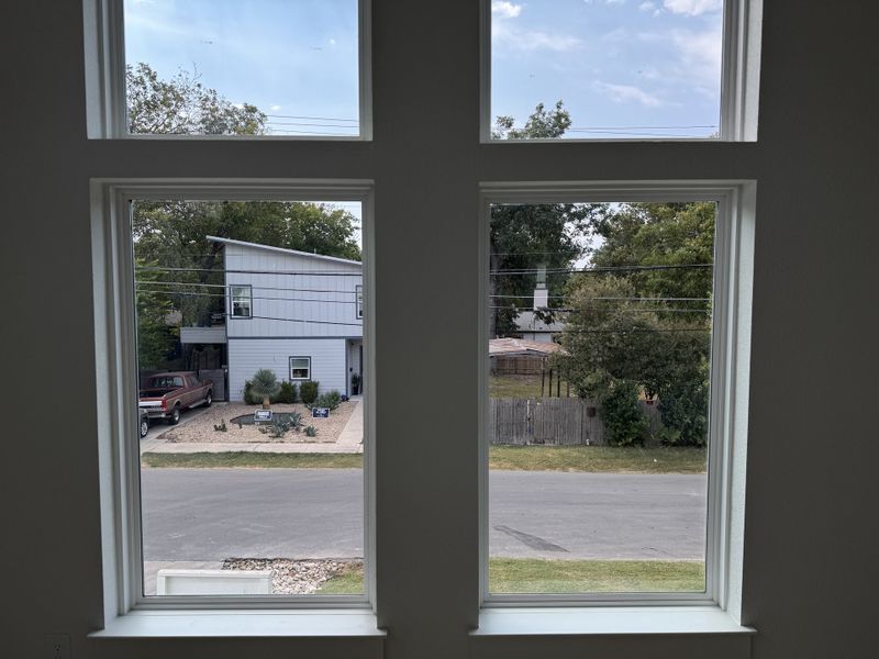 A scenic view through large windows overlooking a modern home with a rustic driveway and green landscape.