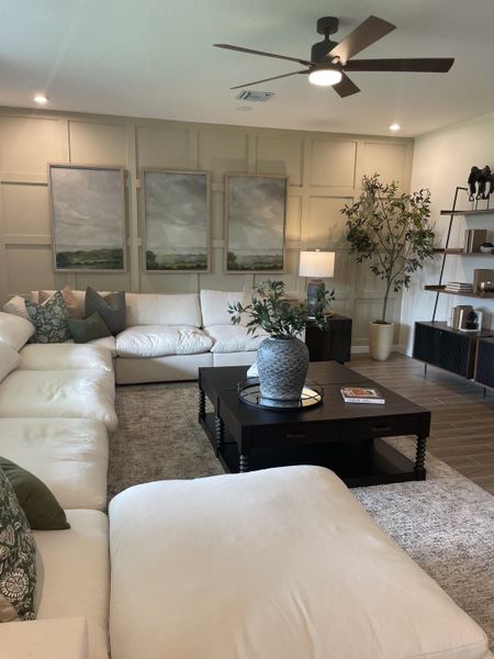 A cozy living room featuring a plush sectional sofa, modern art, and a sleek ceiling fan. Warm and inviting ambiance.
