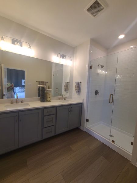 A contemporary bathroom with dual sinks, gray cabinetry, a spacious glass shower, and warm lighting.