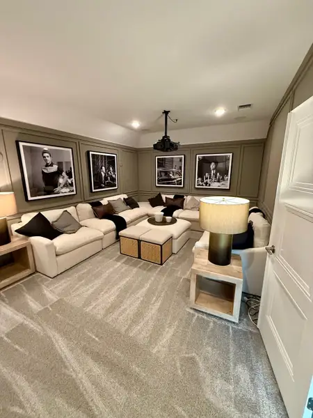 A cozy home theater with plush sectional seating, elegant artwork, and a ceiling projector creates a perfect entertainment space.