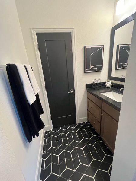 A modern bathroom features geometric floor tiles, wooden vanity, and sleek decor for a stylish and functional space.