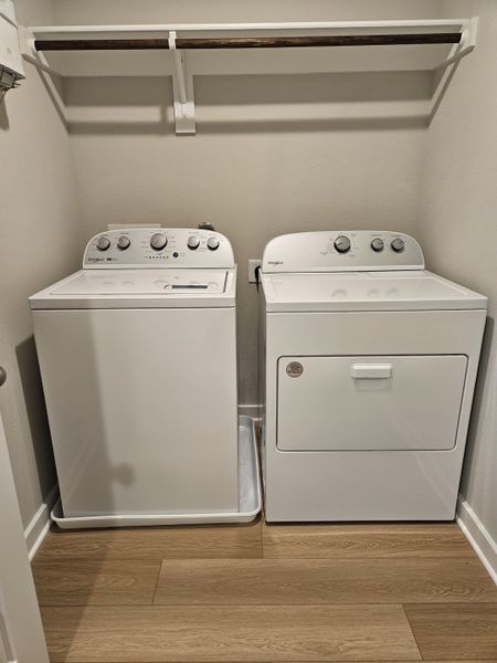 A functional laundry room with white washer, dryer, and a wooden shelf, featuring sleek wood-look flooring. A functional laundry room with white washer, dryer, and a wooden shelf, featuring sleek wood-look flooring.
