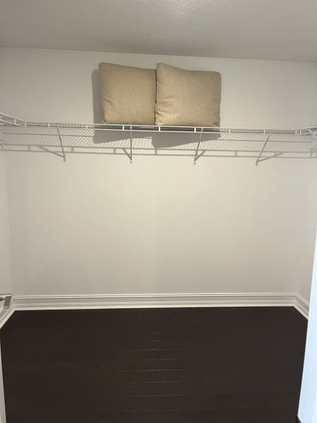A spacious walk-in closet with dark wood flooring and a high shelf, featuring two beige cushions for added style.