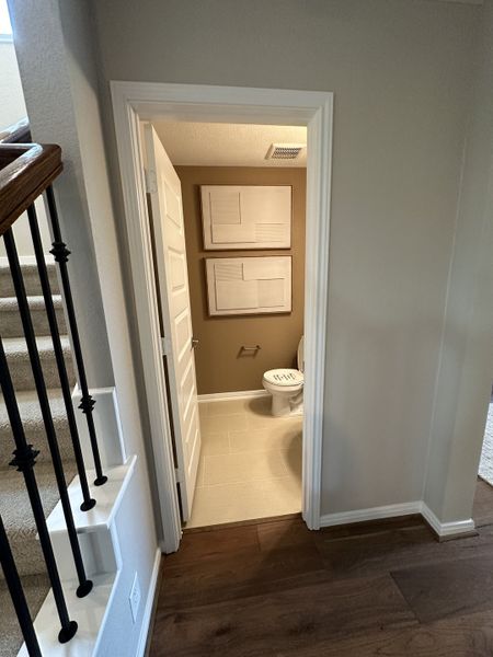A cozy hallway features wooden flooring, a carpeted staircase, and a modern half bath with neutral tones and stylish wall art.