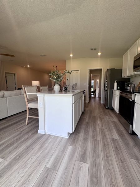 A spacious kitchen with light wood floors, white cabinetry, a sleek island, and modern stainless steel appliances.