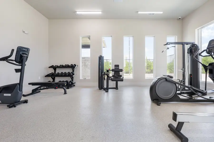 Fitness room with cardio machines, weight rack, and strength equipment on speckled floors with tall windows