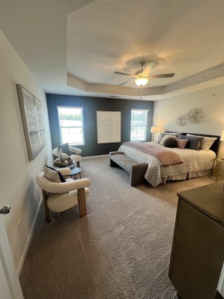 A cozy bedroom featuring a plush carpet, elegant seating area, and a modern ceiling fan with soft lighting.