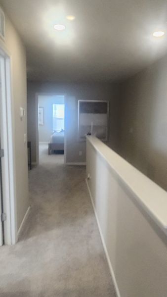 A cozy hallway with soft carpet and recessed lighting leads to a bright bedroom, offering a welcoming ambiance.