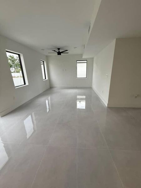 A spacious, open-concept living area with sleek tile floors, large windows, and a modern ceiling fan.